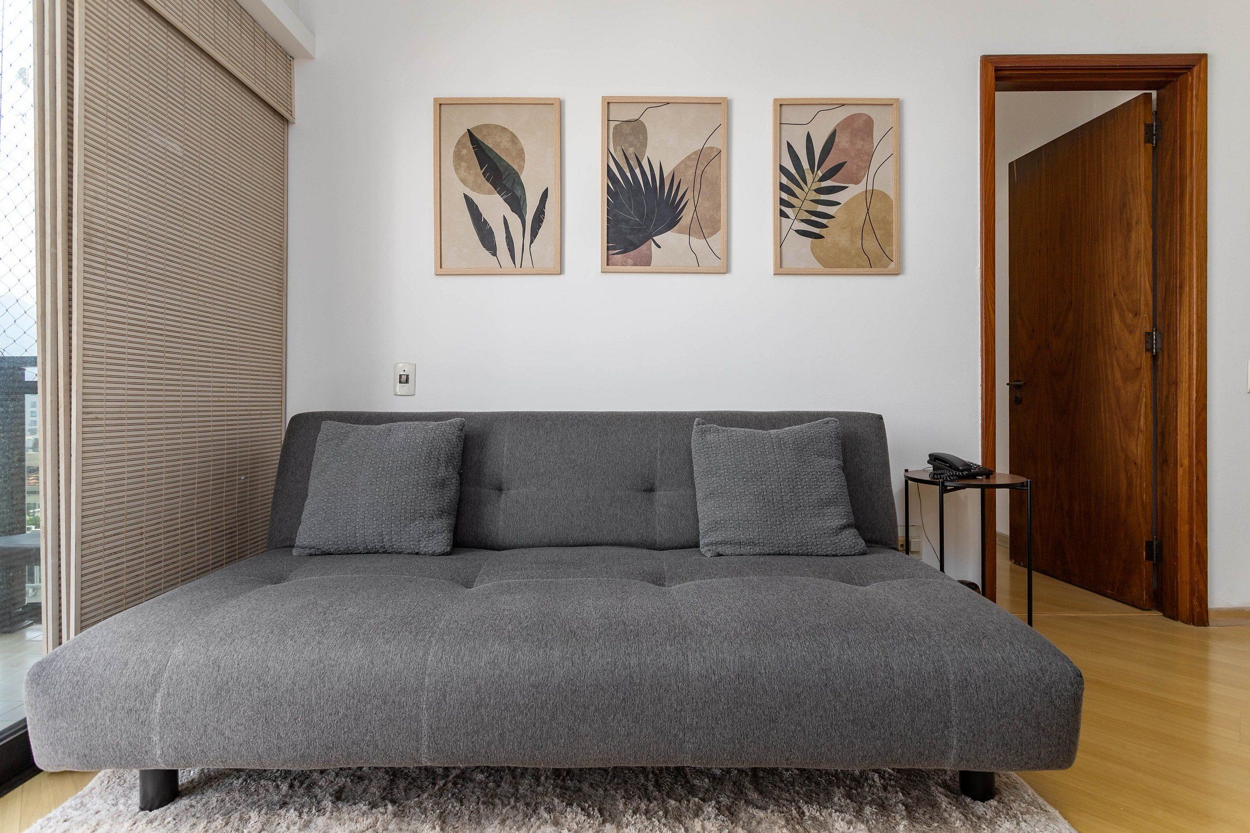 Uma sala de estar moderna com um sofá cinzento, duas almofadas e três impressões botânicas emolduradas na parede.