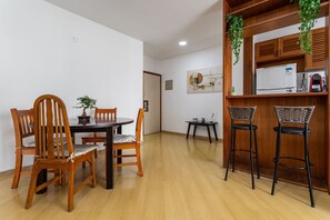 A dining area with a wooden table and chairs, a small kitchen area with a refrigerator and a sink, and a hanging plant. - (1006) Apartamento com 2 Suítes e Vista para o Cristo (Rio de Janeiro)