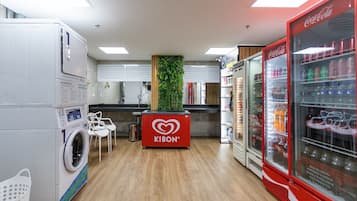 Uma lavanderia com máquina de lavar, balcão com a marca Kibon e geladeira Coca-Cola.