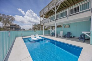 A swimming pool with lounge chairs, a deck with chairs, and a sign welcoming to Sailor's View.