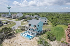 A residential area with a large blue house featuring a balcony, a swimming pool, and a view of a water tower in the background. - 6044- A Sailors View - South Nags Head Escape, Walk to the Beach (Nags Head)