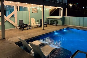 A swimming pool with chairs and a bar area, surrounded by a covered deck with string lights.