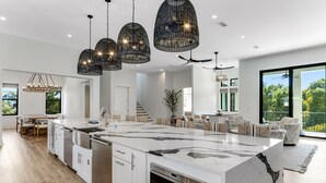 A modern kitchen with a large island, white cabinetry, and black marble countertops. There are pendant lights above the island and a ceiling fan in the dining area. - 🩵🌴 Peaceful Palms | New Build | Heated* Pool & Golf Cart | Free Dolphin Cruise 🐬 (Miramar Beach)