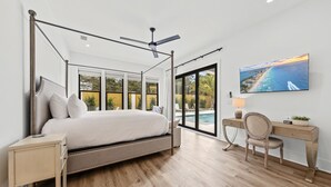 A bedroom with a four-poster bed, a desk with a chair, and a large window overlooking a pool and outdoor area. - 🩵🌴 Peaceful Palms | New Build | Heated* Pool & Golf Cart | Free Dolphin Cruise 🐬 (Miramar Beach)