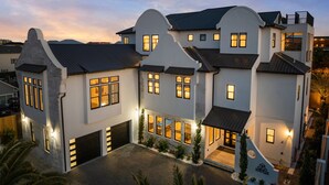 A modern multi-story house with large windows, a garage, and a well-lit driveway. - 🩵🌴 Peaceful Palms | New Build | Heated* Pool & Golf Cart | Free Dolphin Cruise 🐬 (Miramar Beach)