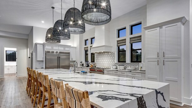 A modern kitchen with a large island, stainless steel appliances, and a dining area with wooden chairs. - 🩵🌴 Peaceful Palms | New Build | Heated* Pool & Golf Cart | Free Dolphin Cruise 🐬 (Miramar Beach)