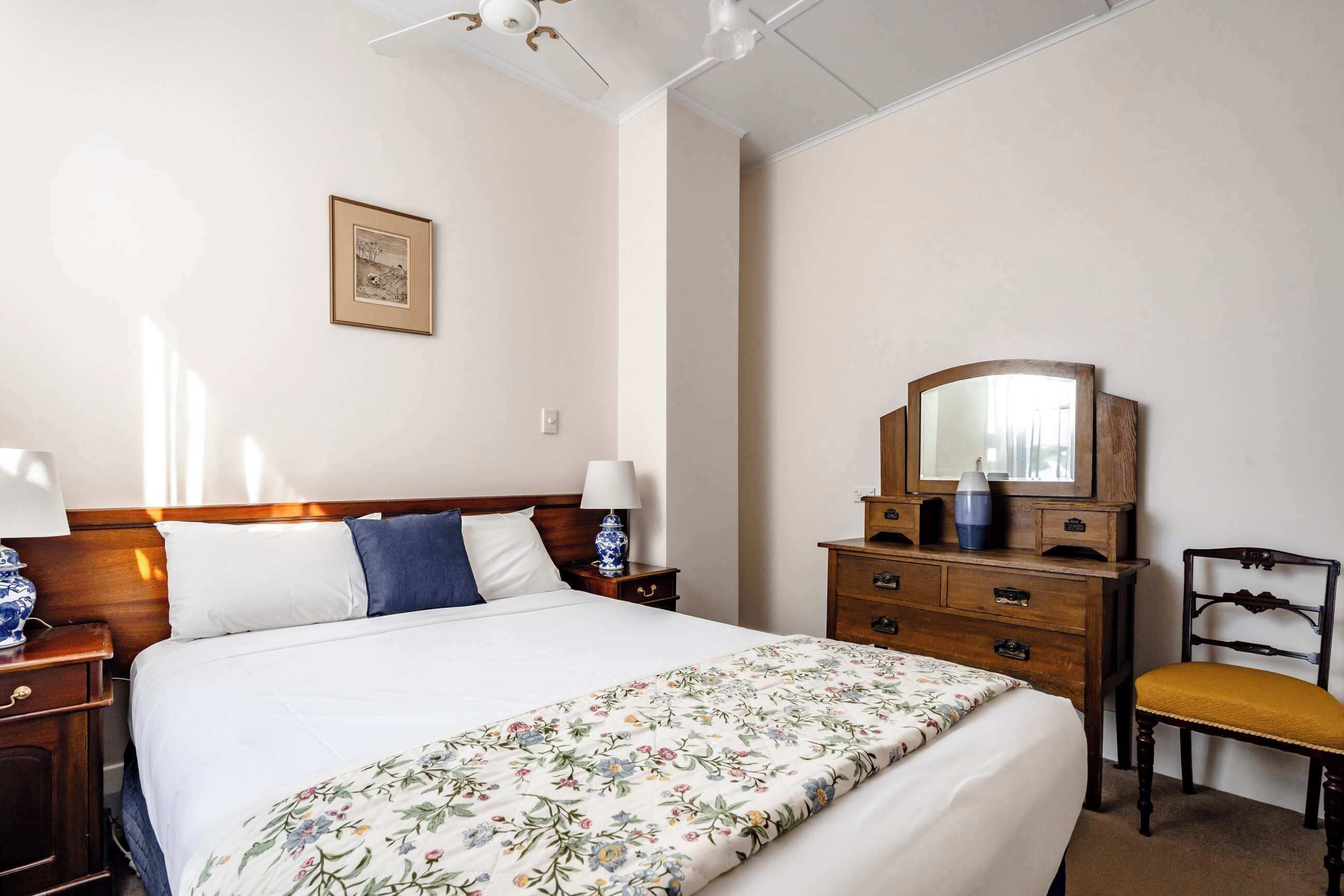 Ein ordentlich eingerichtetes Hotelzimmer mit einem großen Bett, Nachttischen aus Holz, einer Kommode und einem Sessel.