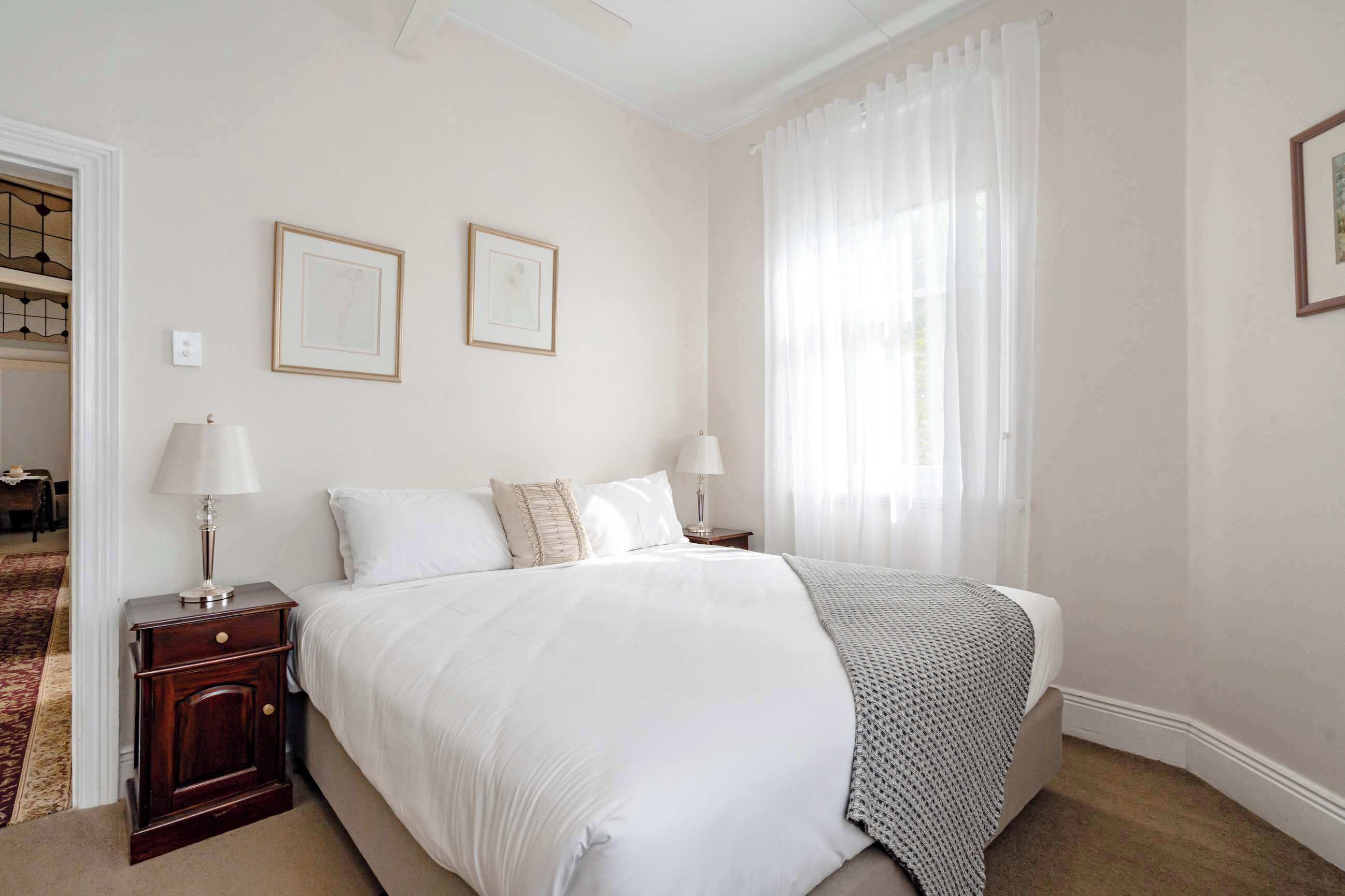 Un dormitorio ordenado con una cama grande, dos mesitas de noche con lámparas y dos cuadros enmarcados en la pared.