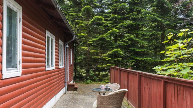 A wooden cabin with a porch, a table, and two wicker chairs. - 2 bedroom amazing home in Kolind (Kolind)