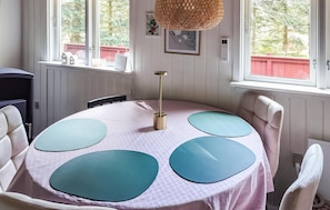 Et rundt bord med et pink borddække og fire blå stole, en hængende lampe og et vindue med udsigt til træer.