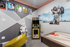 Quarto com decoração temática de Star Wars, incluindo cartazes, uma figura em tamanho real de Stormtrooper e um jogo Multi Arcade.