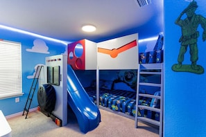Uma cama box com escorrega, escada e prateleira com brinquedos.