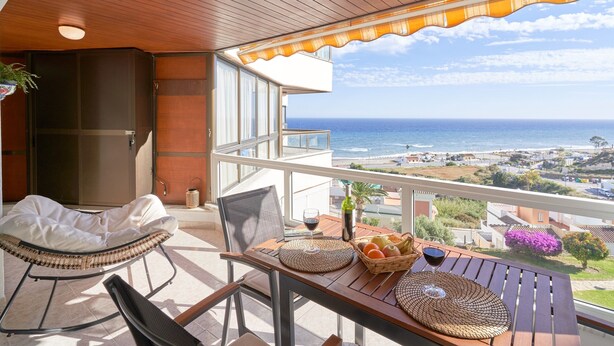 A balcony with a view of the ocean, a wicker chair, a table with a basket of fruit and wine glasses, and a wooden ceiling. - Apartment 'Laolita' with Sea View, Wi-Fi and Air Conditioning (Torrox)