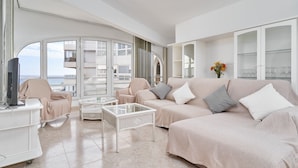 A spacious living area with a large sofa, a coffee table, and a television on a white stand. There are large windows with a view of the sea. - Apartment 'Laolita' with Sea View, Wi-Fi and Air Conditioning (Torrox)