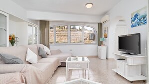 A living room with a sofa, a glass coffee table, a TV on a stand, and a large window with a view of a hillside. - Apartment 'Laolita' with Sea View, Wi-Fi and Air Conditioning (Torrox)