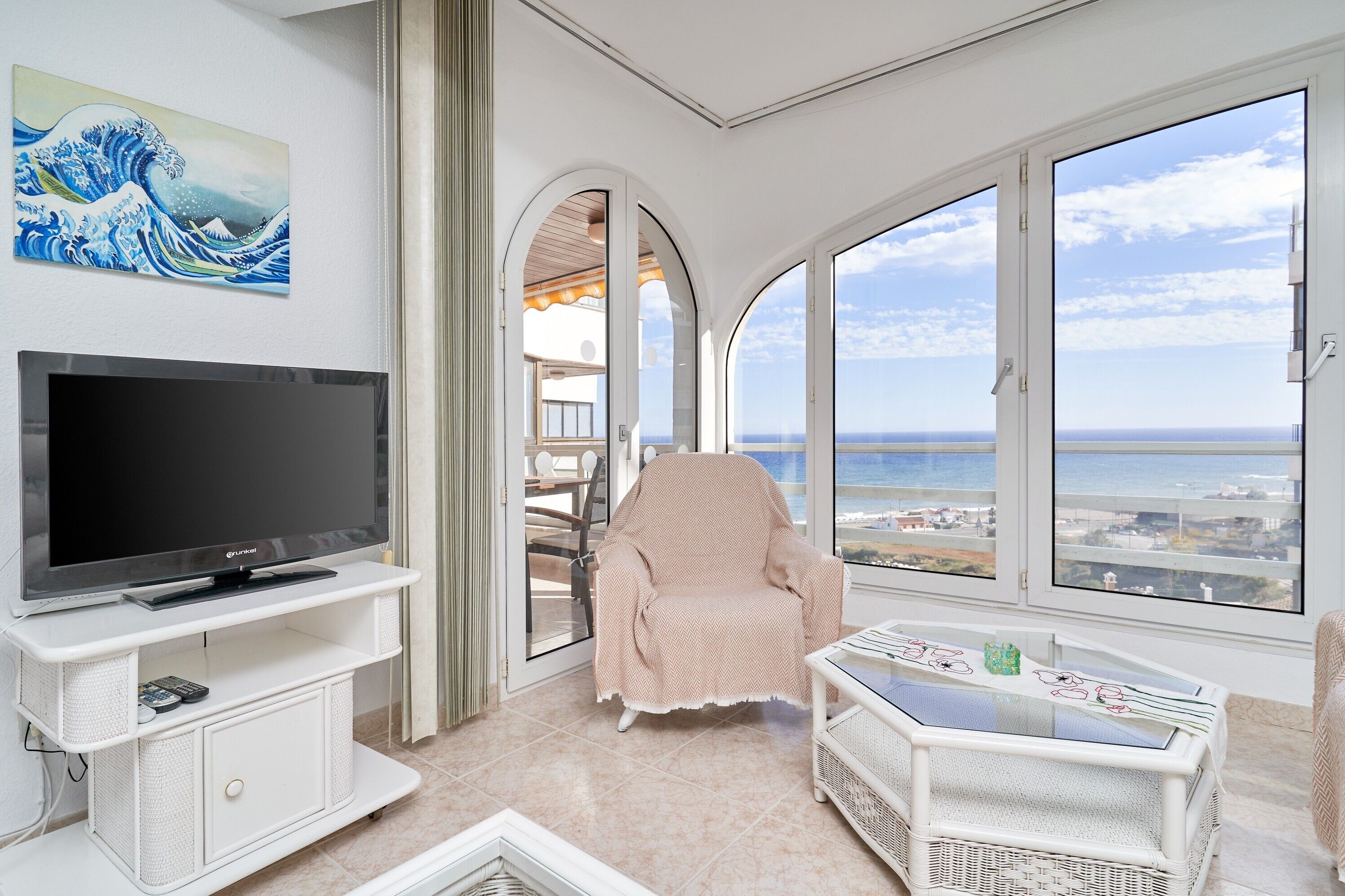 Une chambre avec une télévision, une chaise, une table et une vue sur la mer.