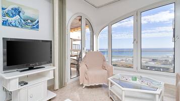 Une chambre avec une télévision, une chaise, une table et une vue sur la mer.