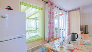 A kitchen with a refrigerator, table with tablecloth, chairs, and a window with curtains.
