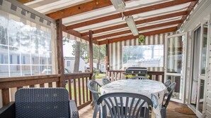 A covered deck with a table and chairs, a grill, and a view of the backyard.