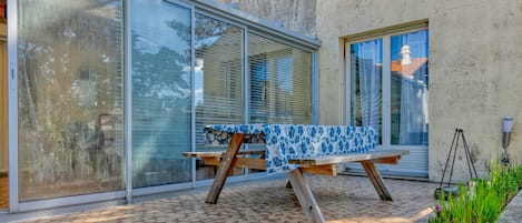 Un patio con una mesa y sillas, un muro de hormigón y un amplio ventanal corredero de vidrio.