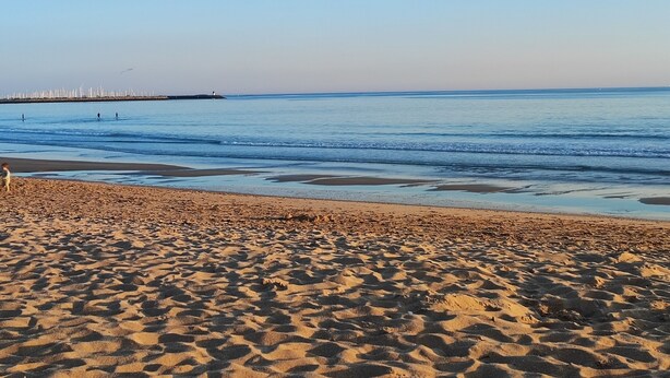 Ein Sandstrand bei klarem Himmel und ruhiger See.