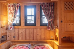 Une pièce en bois avec un lit, deux fenêtres et des rideaux.