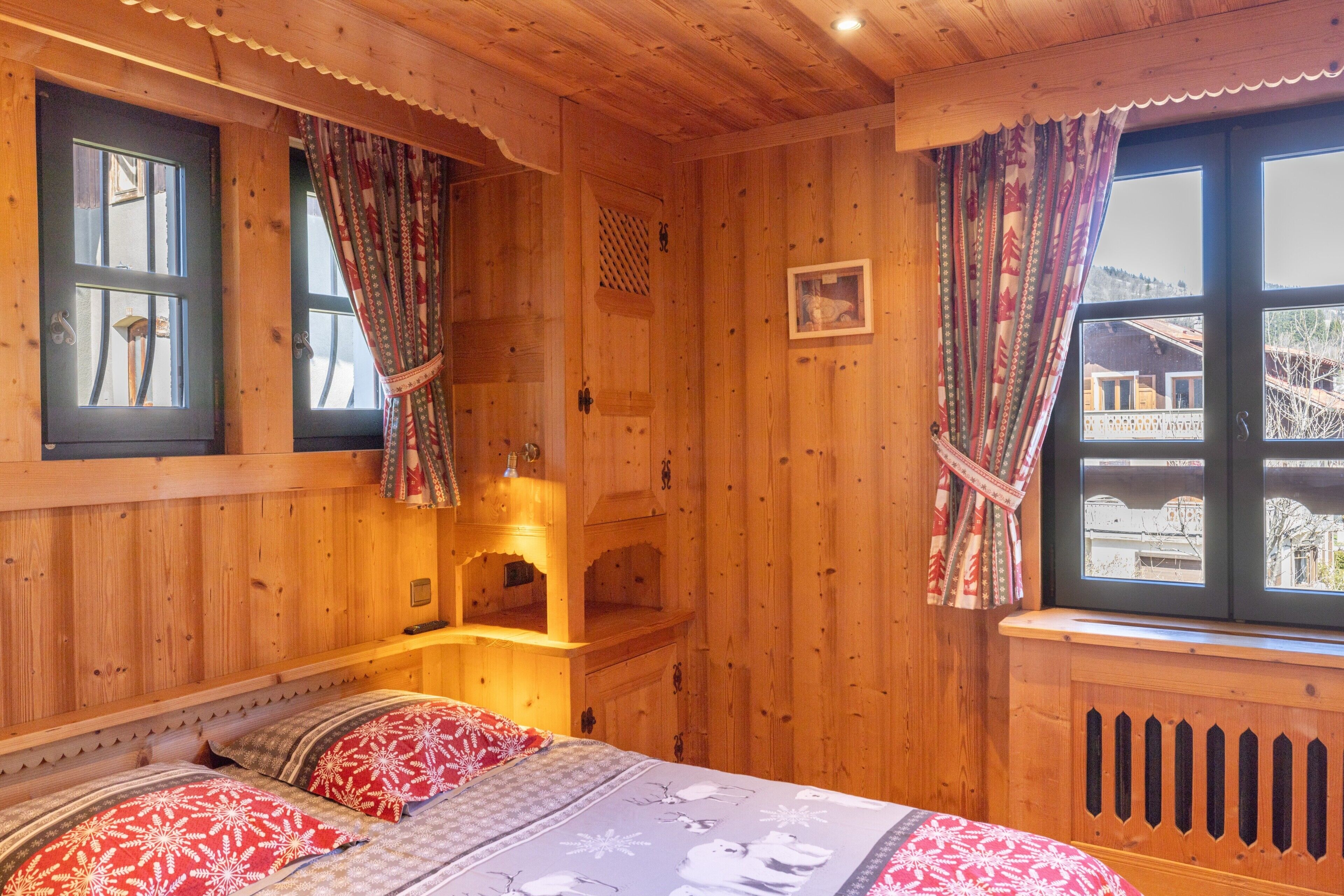 A wooden room with a bed, a window with curtains, a shelf, and a picture on the wall.