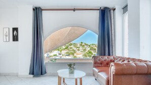 A room with a large arched window, a leather sofa, a small round table, and a potted plant. - Holiday Home 'Brandy' with Sea View, Wi-Fi and Air Conditioning (Calpe)
