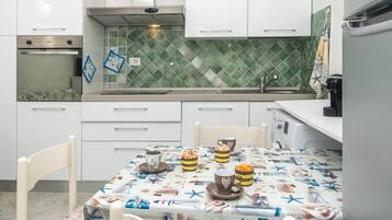 Eine Küche mit weißen Schränken, einer gefliesten Spritzschutzwand und einem Tisch, gedeckt mit einer Tischdecke im Marine-Stil.