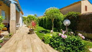 Ein Gartenweg führt zu einem Gebäude mit einer Pergola, Blumentöpfen und einer Laterne.