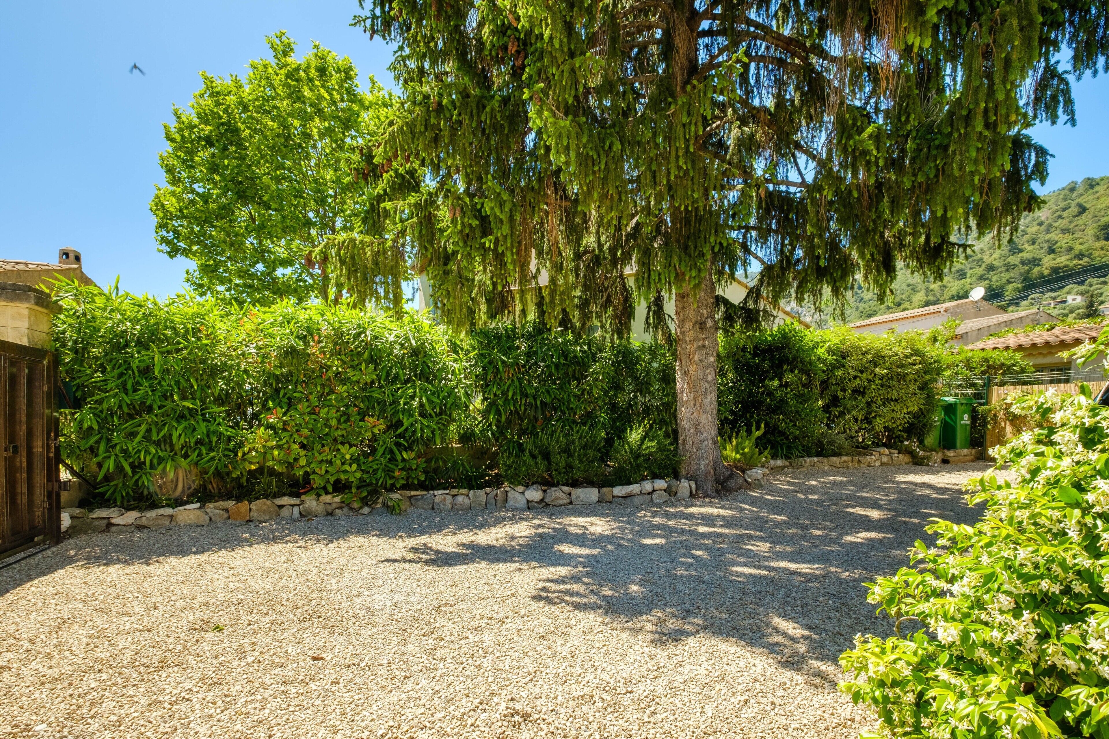 A gravel driveway leading to a house with a stone wall and lush greenery.