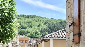 A narrow alleyway with stone buildings, a wooden staircase, and a view of a forested hill.