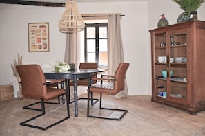 Zona pranzo con tavolo, sedie, lampadario, finestra con tende e credenza con stoviglie.