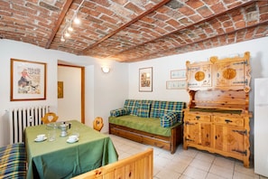 A cozy room with a brick ceiling, a green sofa, a wooden cabinet, and a dining table set with glasses and plates.