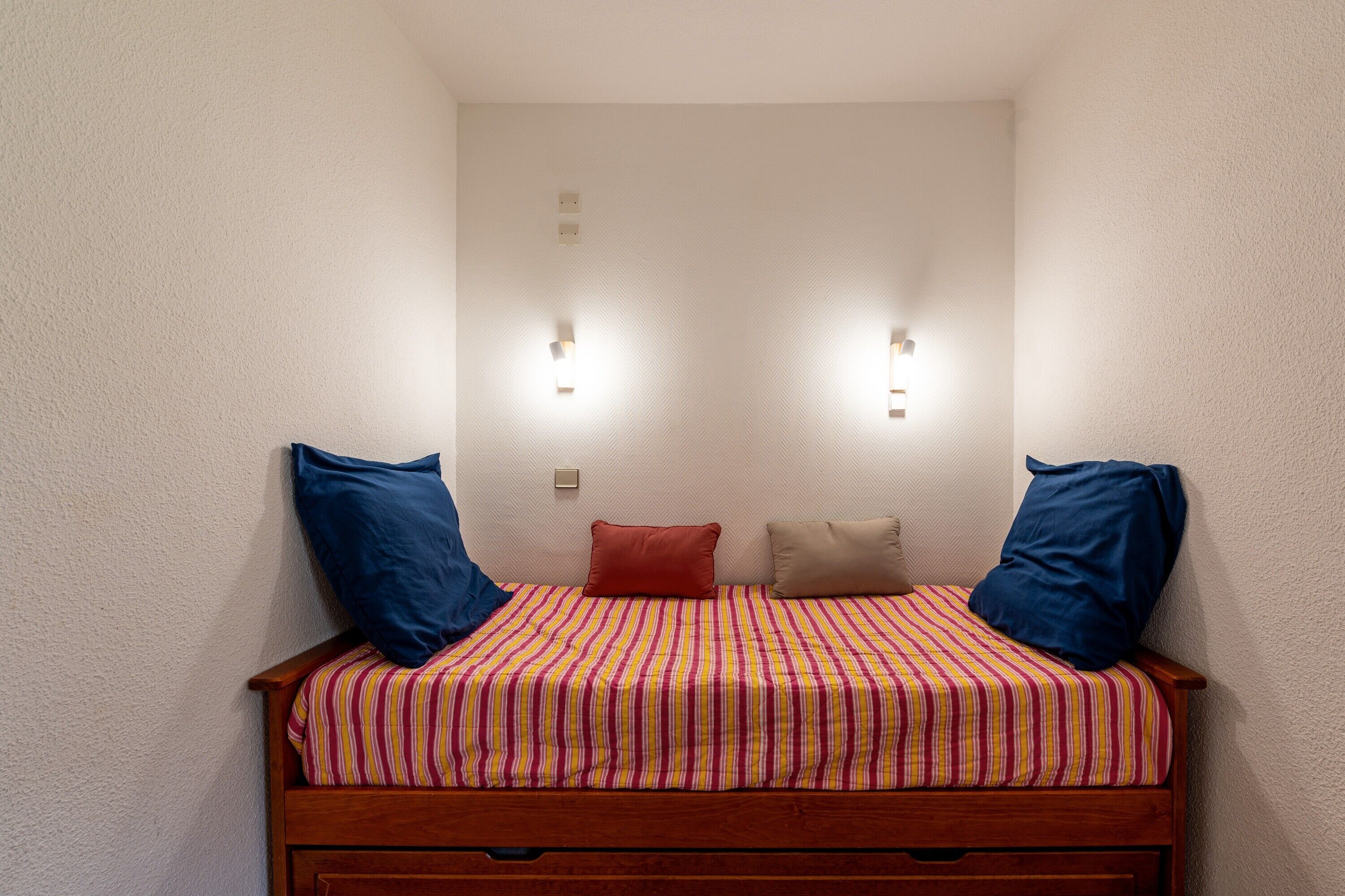A single bed with a striped bedspread, two wall-mounted lights, and pillows on either side.