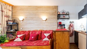Ein gemütliches Zimmer mit einer Holzsofa, einem kleinen Tisch und einer Küchenzeile mit einem Regal und einer Kaffeemaschine.