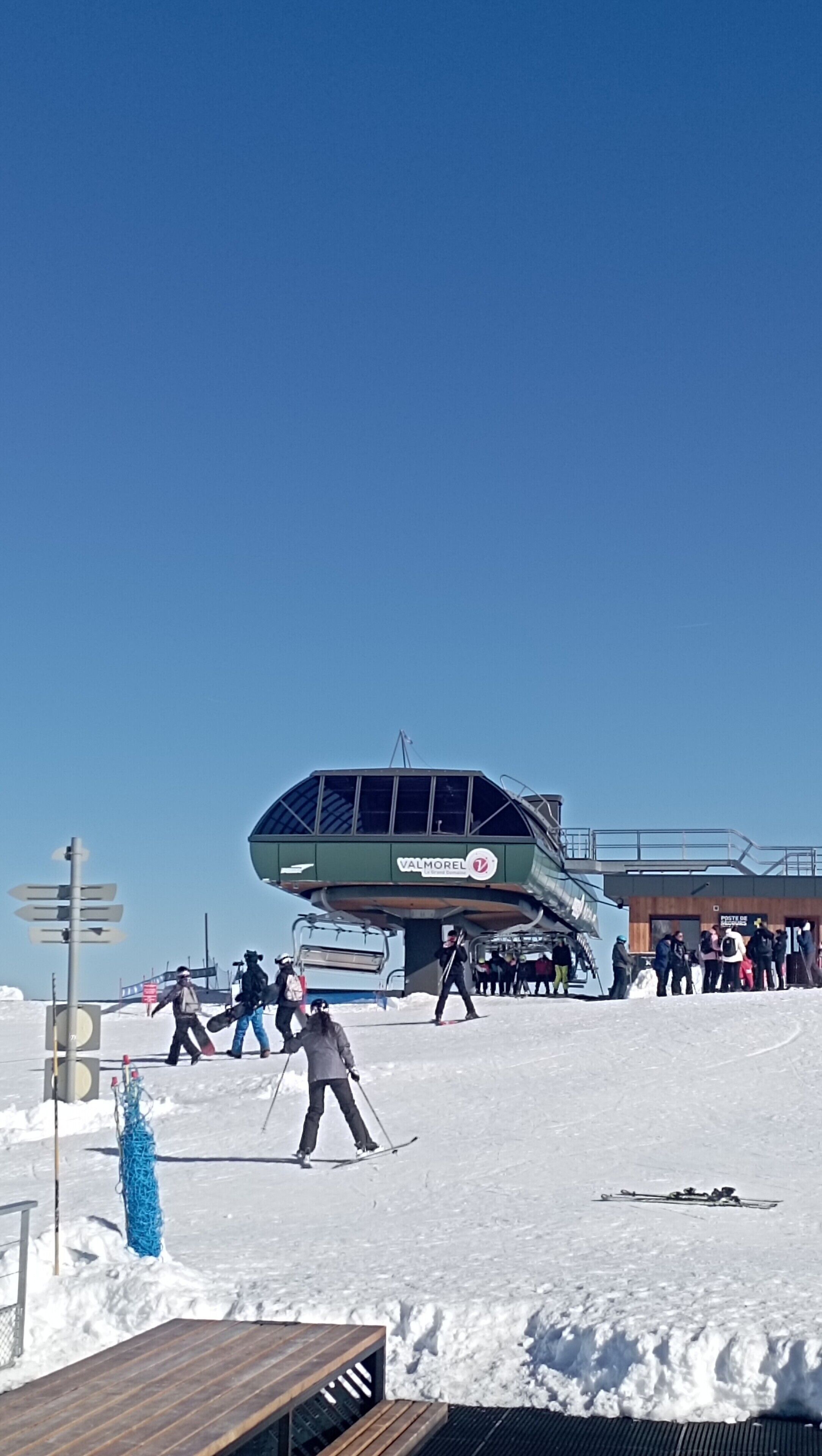 Eine Seilbahn mit wartenden Personen, ein Holzboden und ein Schild für Valmorel.