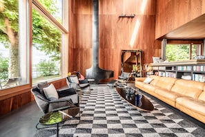 Moderni olohuone, jossa on takka, suuret ikkunat, ruutukuvioinen lattia ja nahkasohva.