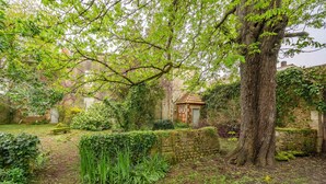 Un jardin avec un mur de pierre, un arbre et un bâtiment doté d’un toit rouge.