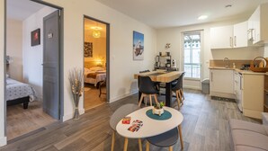 Espaço compacto com área de refeições, kitchenette e quarto com cama e mesa de cabeceira.