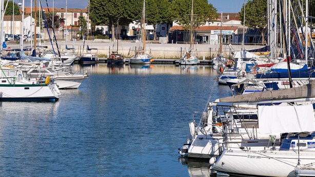 Marina com vários veleiros atracados, cúpula de igreja ao fundo e céu claro.