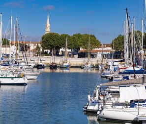 Un port de plaisance où sont amarrés de nombreux voiliers, une église dont le clocher se détache à l’arrière-plan et un ciel dégagé.