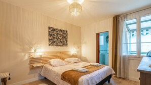 Quarto com cama, luminárias de cabeceira, um quadro, janela com cortinas e vista para o exterior.