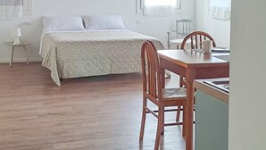 Habitación con techo de madera, cama con ropa blanca, mesa de comedor con sillas y ventana con cortinas.
