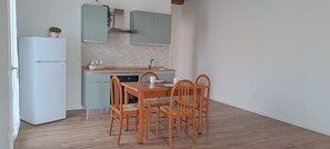 Een compacte keuken met een witte koelkast, een houten eettafel met vier stoelen, en een klein aanrecht met een spoelbak.