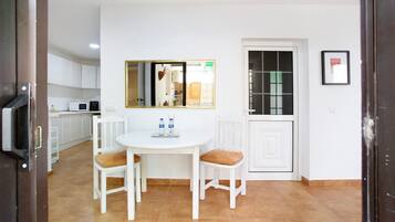 Une cuisine compacte avec des meubles blancs, une table à manger blanche accompagnée de deux chaises, et une fenêtre donnant sur l’extérieur.