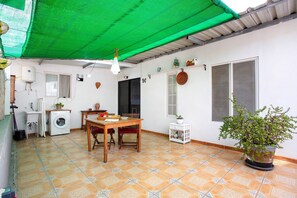 A room with a washing machine, a table with chairs, a potted plant, and a green canopy.
