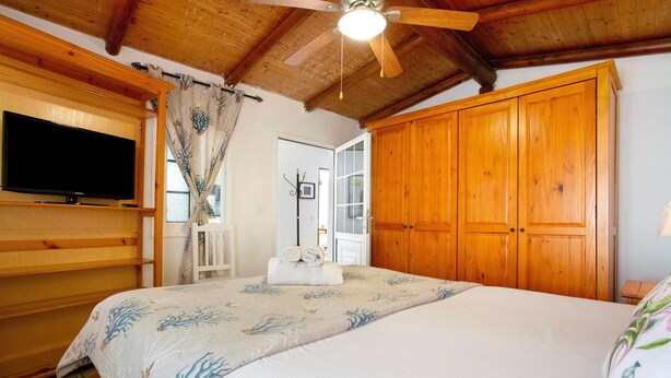 Une chambre à coucher comprenant un lit, une armoire en bois, un téléviseur et un ventilateur de plafond.
