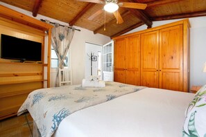 Un dormitorio con cama, armario de madera, televisor y ventilador de techo.