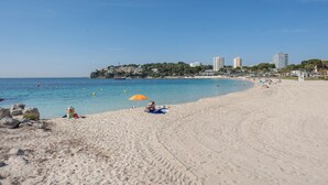 A beach with a clear sky, sandy shore, and buildings in the background.
